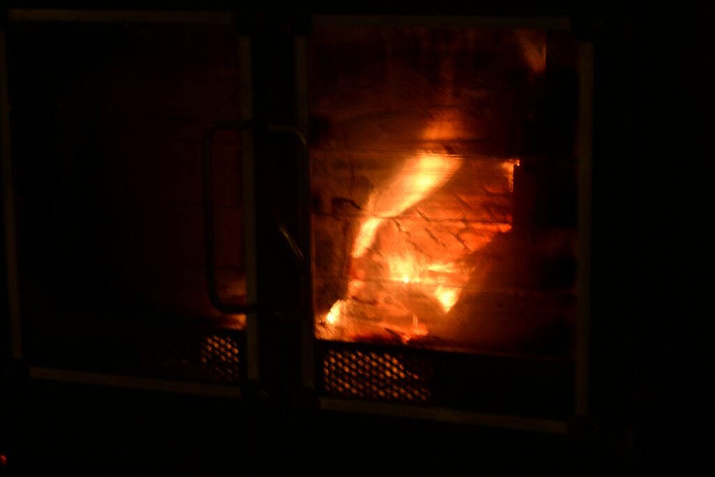 Glastür eines Kaminofens mit Feuer dahinter in einem dunklen Raum