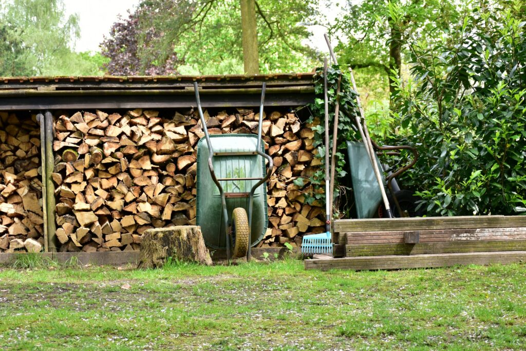 Offener Holzunterstand mit Pultdach im Garten, davor eine grüne Schubkarre