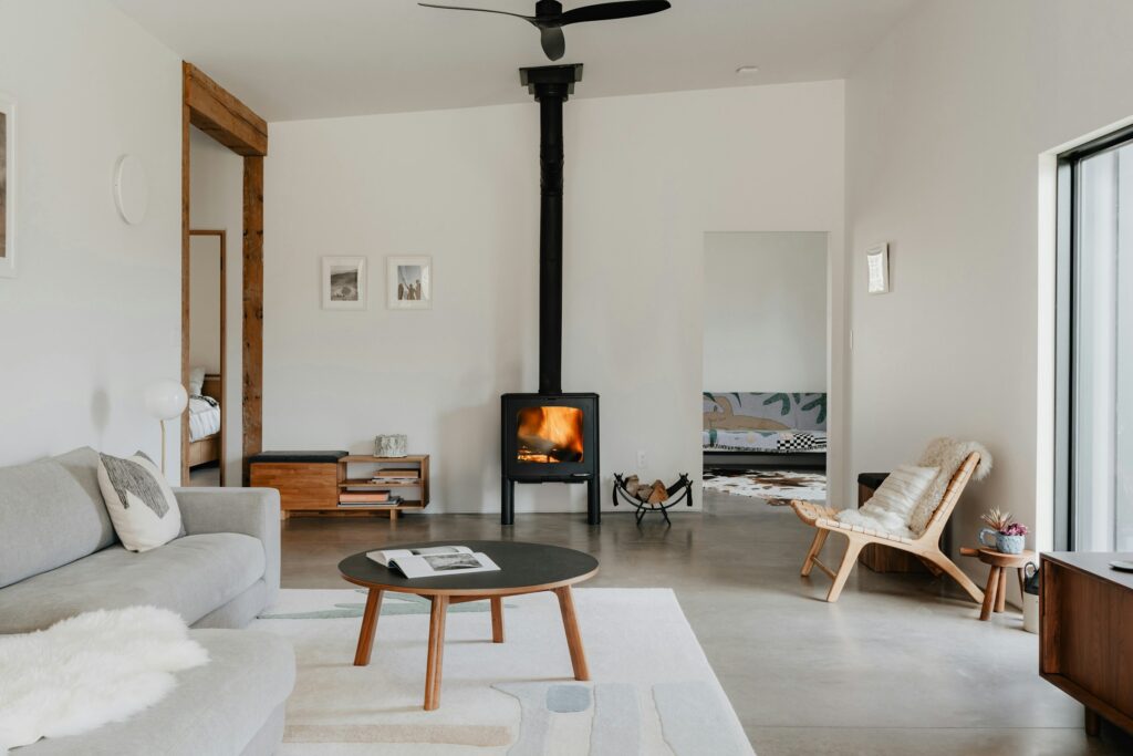Schwarzer Kaminofen mit Feuer und langem Ofenrohr in einem hellen Wohnzimmer mit Sofa und Couchtisch